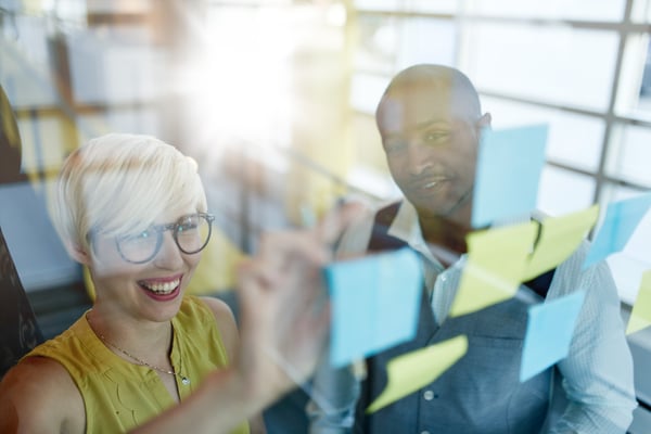 Two creative millenial small business owners working on social media strategy brainstorming using adhesive notes in windows